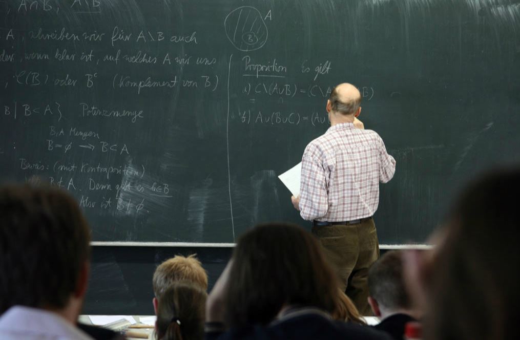 Back of a teacher writing on a chalkboard.