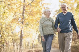 Elderly couple walking on a trail amongst trees with colorful fall leaves