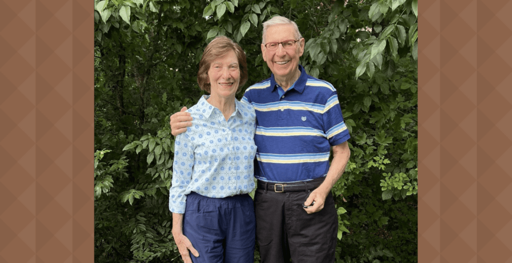 Ron Braun and his wife pose for a photo in front of greenery