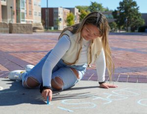 Girl sits on the ground and writes with chalk on campus.